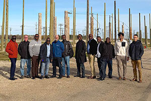 A group of men pose for a photo in front of hydro poles at a training facility.