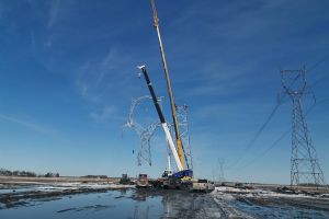 A large crane moving a transmission tower into position during construction.