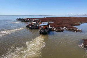 An arial photo of boats pushing back against and floating island of peat at the Keeyask Generating Station.