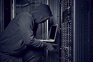 A hacker using a laptop in a server room.