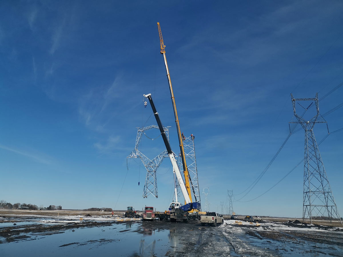 A large crane moving a transmission tower into position during construction.